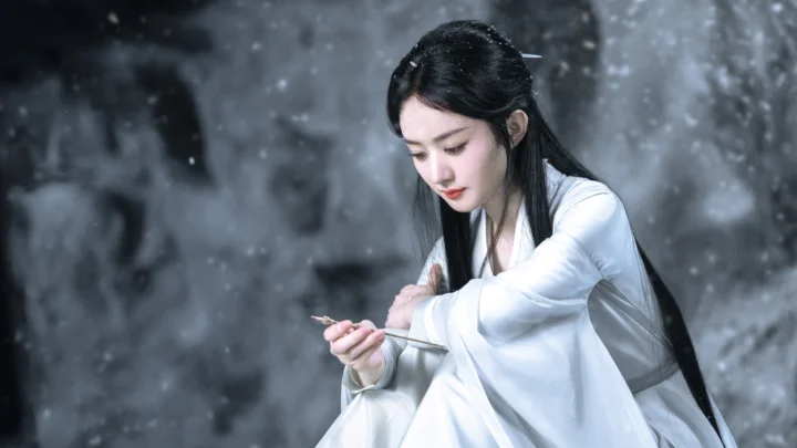 一名身穿白色长袍的女子坐在灰暗的雪景中。
