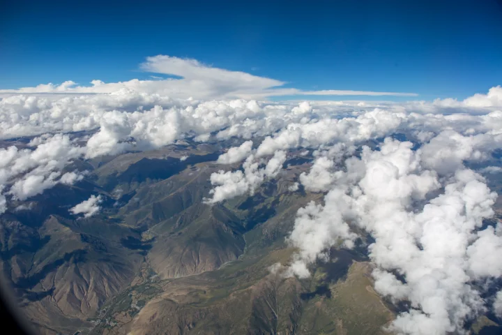 从高空俯瞰群山与翻涌的云层，远处铺展着晴朗的蓝天。