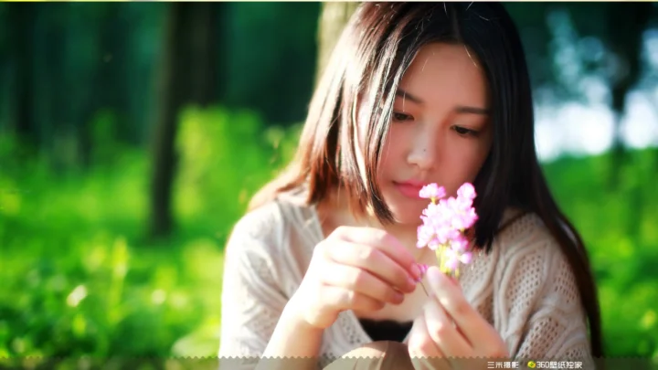 一名女子在绿色户外环境中低头手捧粉色花朵。
