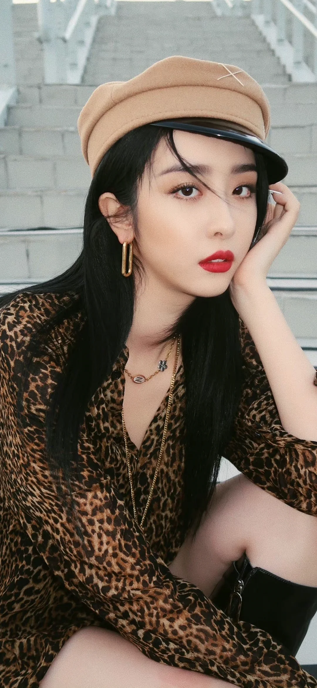 茶色の帽子とヒョウ柄のトップスを着た成人女性が、階段の前でカメラを見つめています。