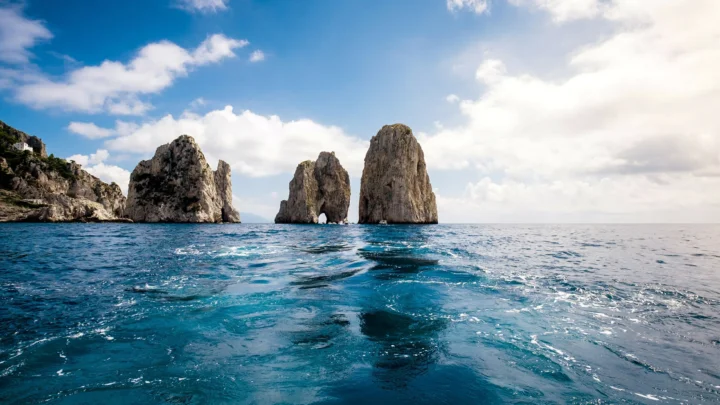 海面上矗立着几座巨大的岩石，远处是湛蓝天空与白云。