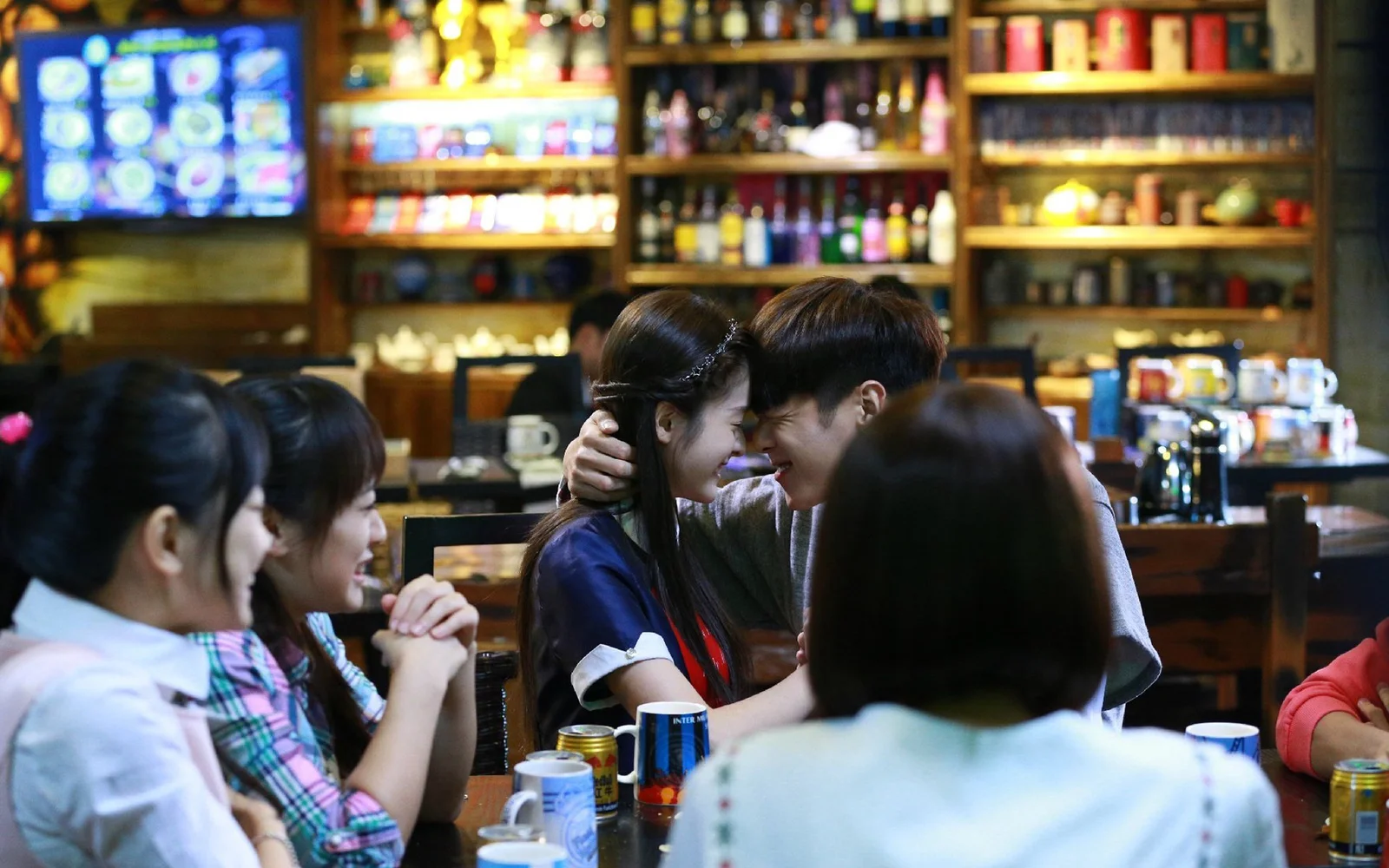 여러 사람이 카페 테이블에 둘러앉아 있고 중앙의 두 사람이 가까이 앉아 있습니다.