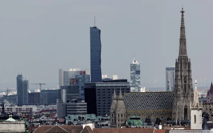 城市天际线中可见一座带有彩色几何屋顶的哥特式教堂，以及周围的现代高层建筑。