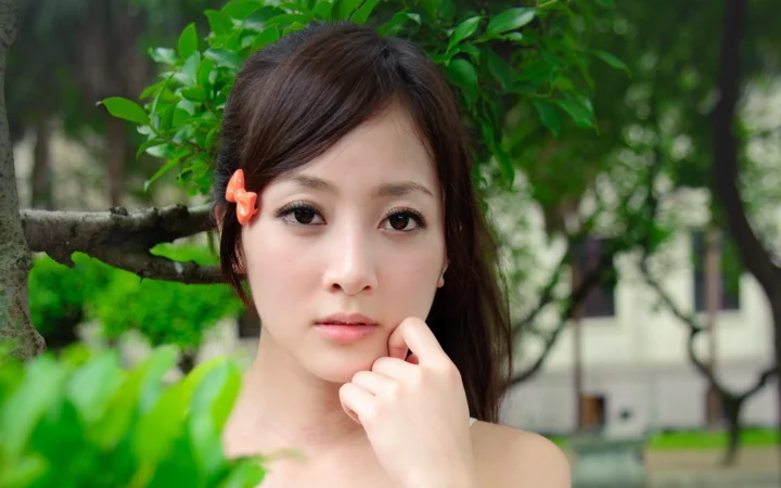 一位成年女性在绿叶背景前看向镜头，并用手轻触下巴。