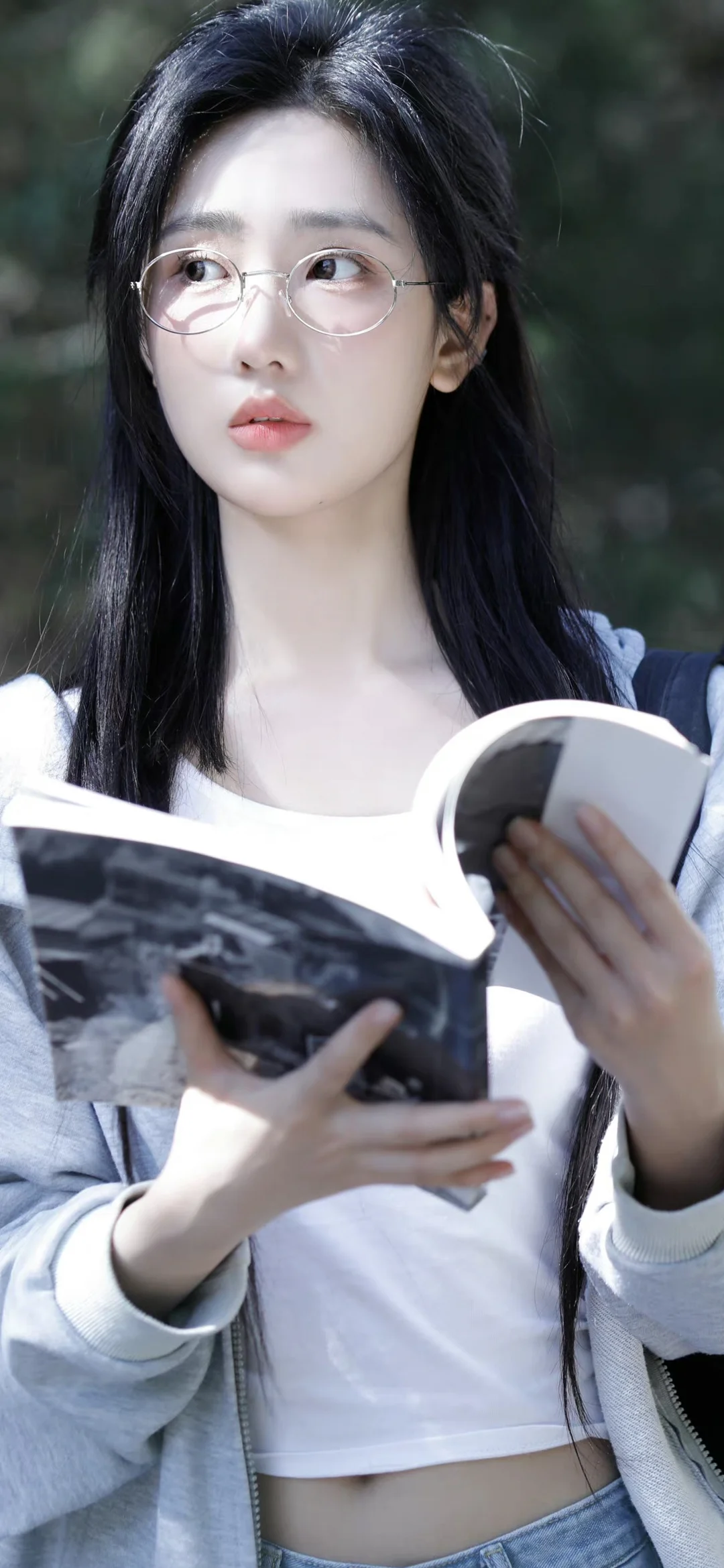 一名戴眼镜的女性在户外手持书本阅读。