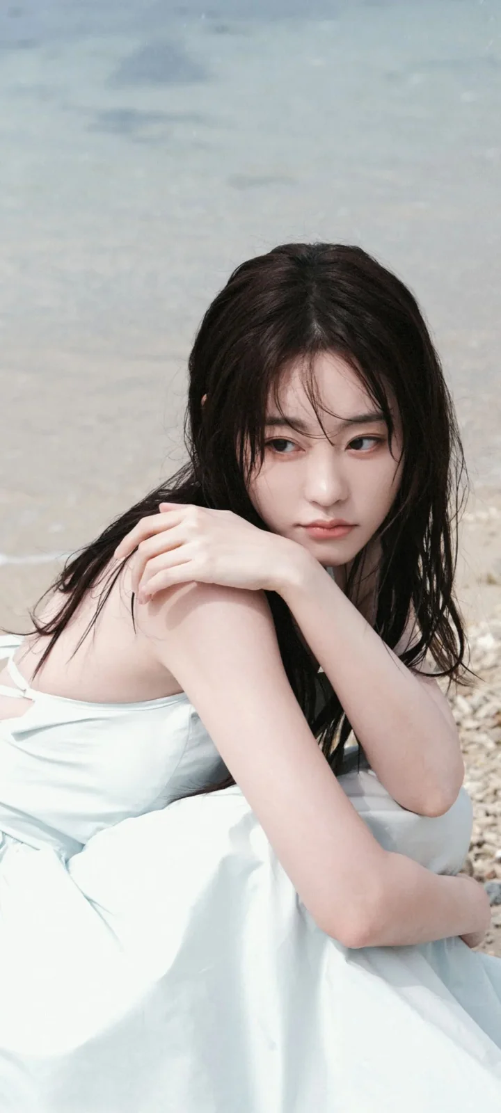 一名長髮女子坐在海邊的淺色布料上，濕髮垂落在肩頭。