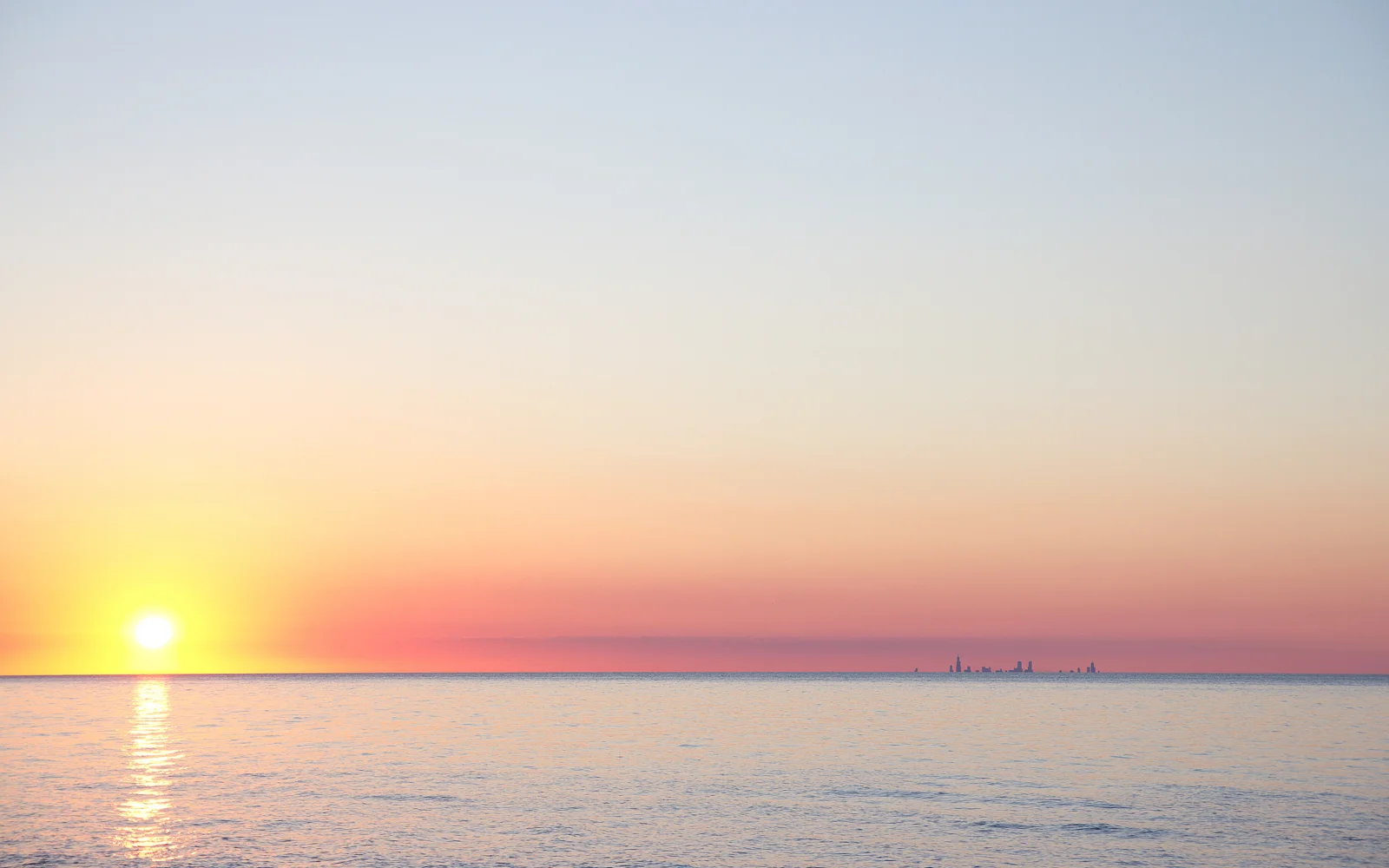 夕阳贴近海平线，金色光芒映照着平静的海面，远处隐约可见城市天际线。