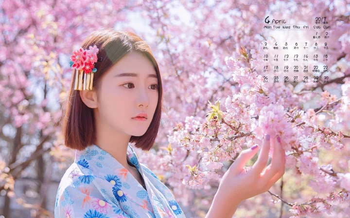 一名成年女性站在盛开的粉色樱花旁，手边轻触着花枝。