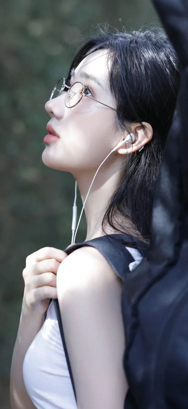 一名戴圆框眼镜并佩戴有线耳机的黑发女子侧脸望向上方。