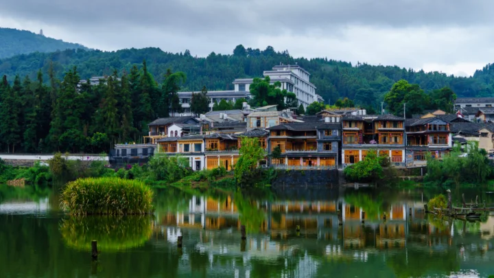 湖面倒映着山林、层叠民居与远处建筑，构成宁静的山水村落景色。