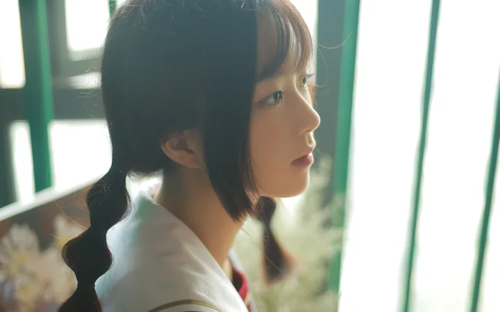 一名女子在明亮窗边呈侧脸，留着编发并穿着白色上衣。