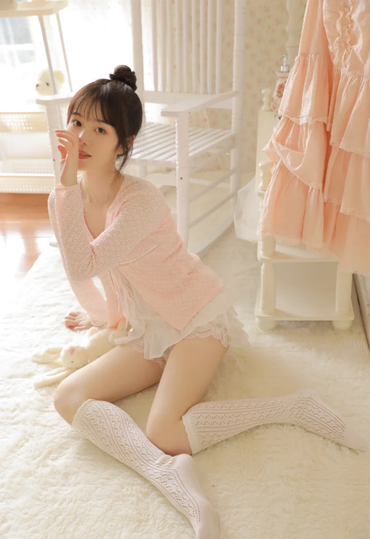 一名成年女性坐在明亮温馨的室内地毯上，身穿粉色针织上衣和白色过膝袜。