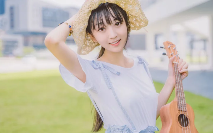一名戴草帽的女子身穿白色上衣，在户外草地上手持尤克里里。