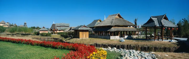 蓝天下的传统木结构建筑群前是整齐的红色花卉、草地和石景。