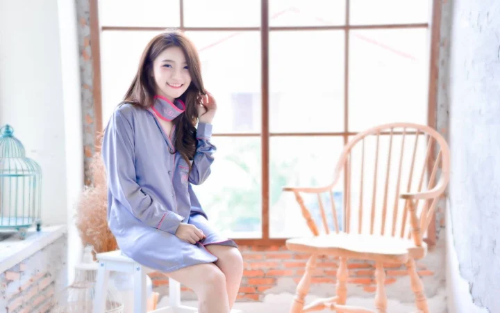 연한 파란색 옷을 입은 여성이 밝은 창가에 앉아 미소 짓고 있습니다.