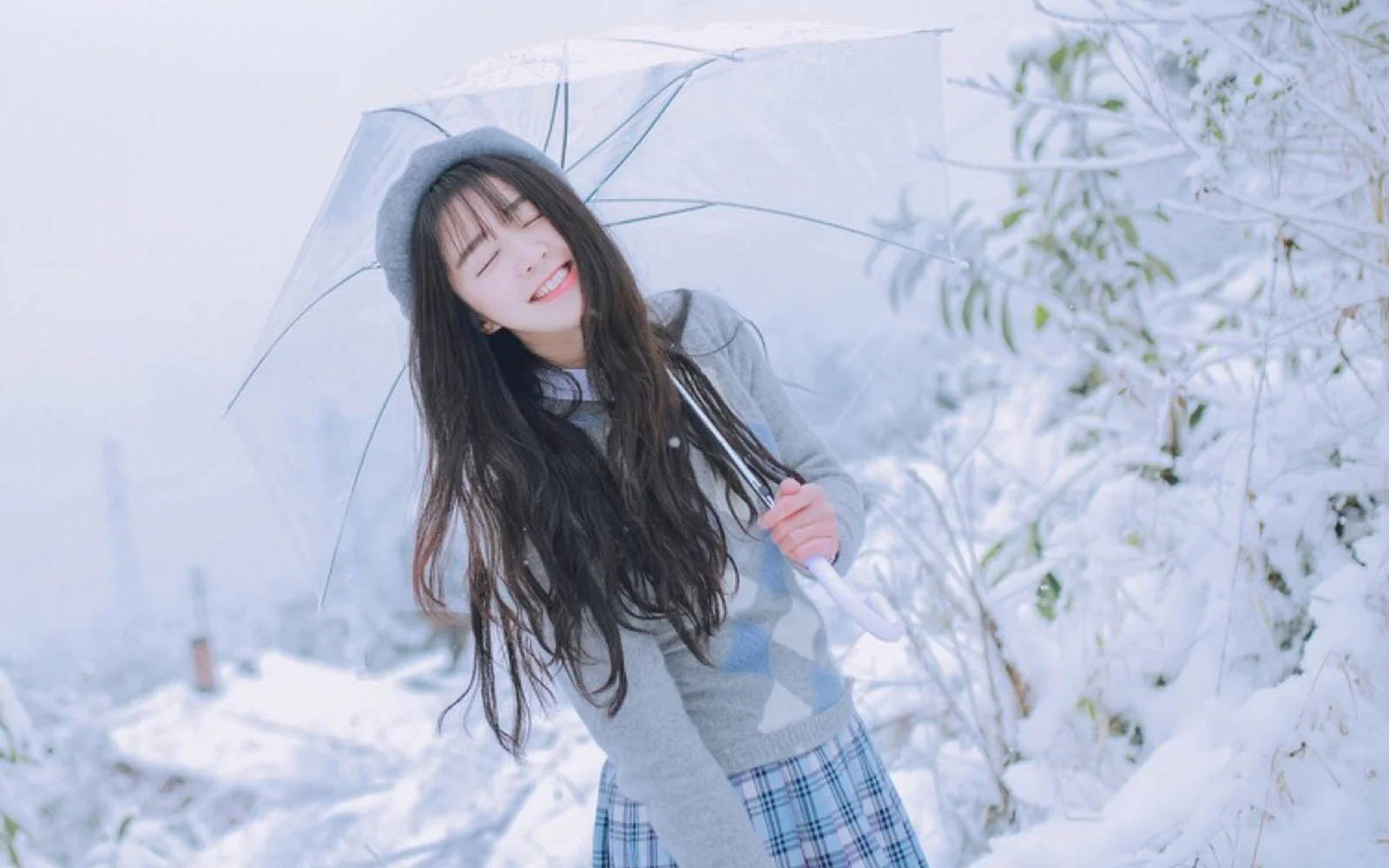 一名女子在白雪覆盖的户外撑着透明雨伞微笑。