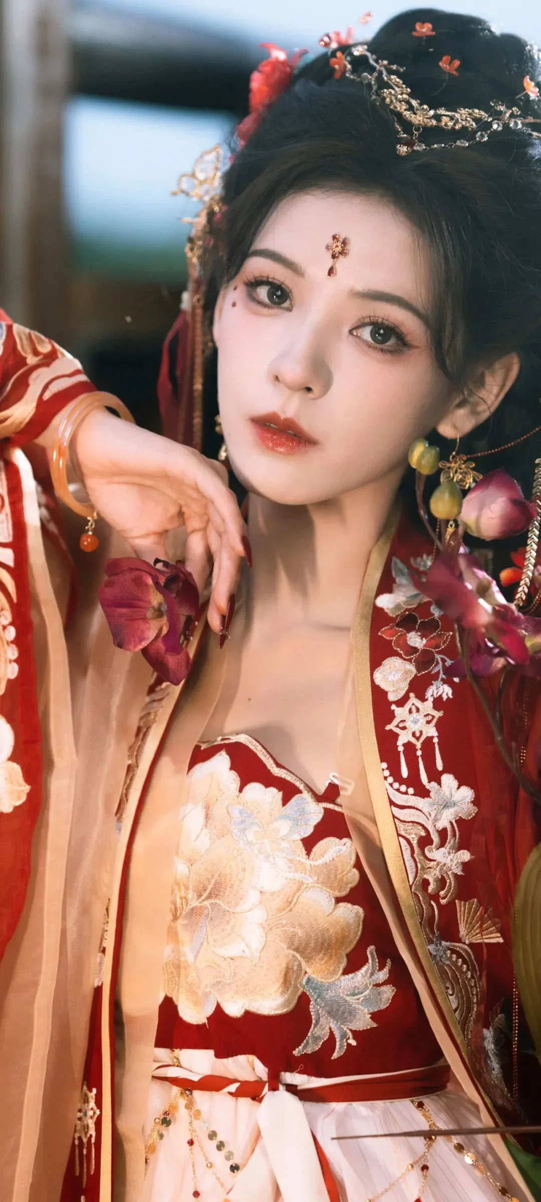 붉은 전통 의상과 화려한 머리 장식을 한 여성이 카메라를 향해 포즈를 취하고 있다.