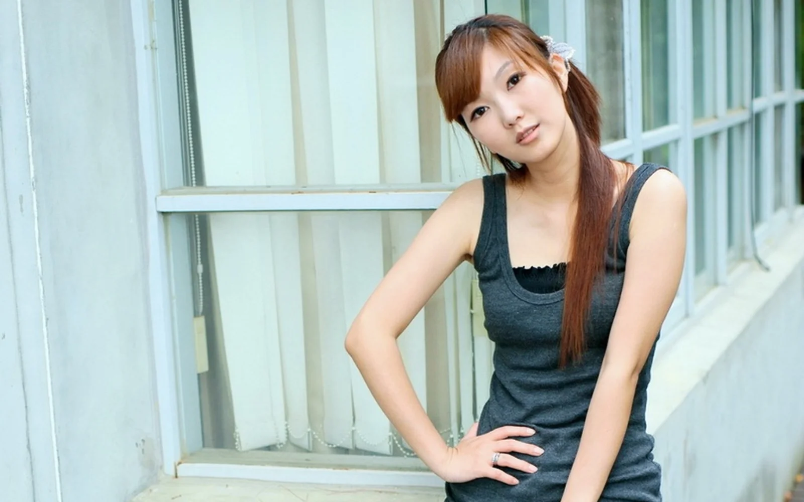 一名长发女性穿着深色背心坐在窗边。