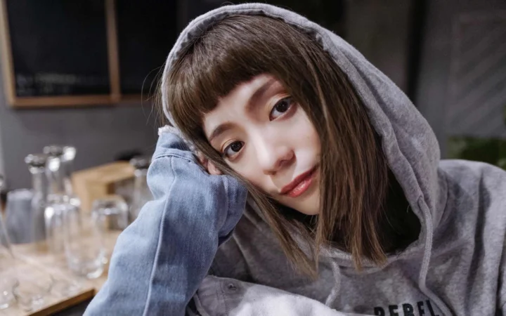 一名成年女子穿着灰色连帽衫，靠着手臂注视镜头。