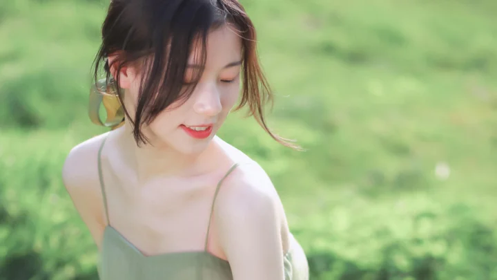 一名黑发女子在绿色草地背景前低头微笑。