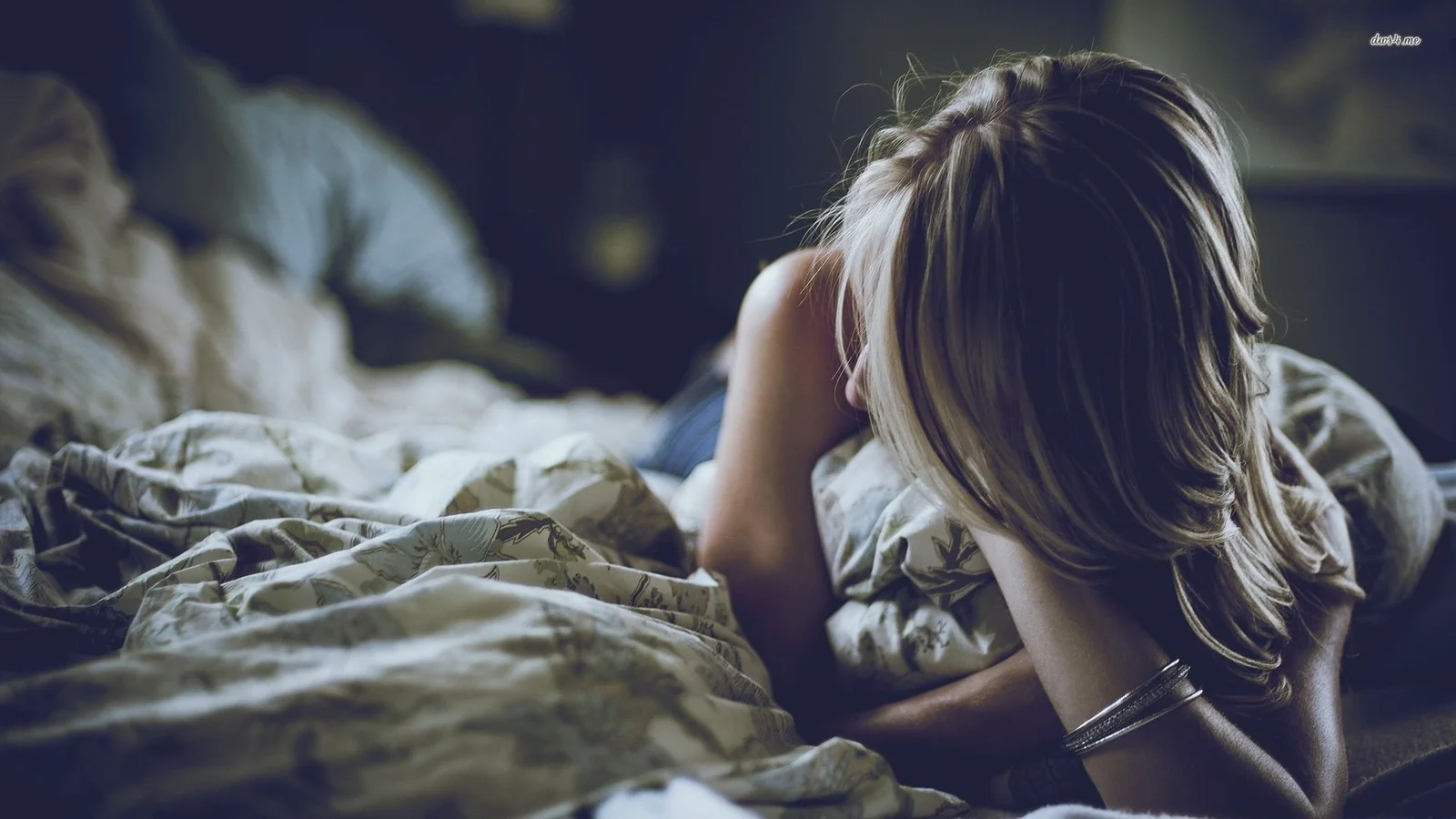 一名金髮女性背對鏡頭趴在鋪著床品的床上。
