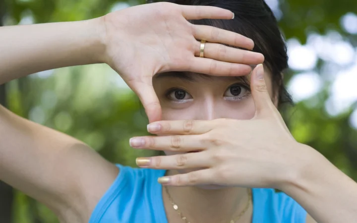 一名穿蓝色上衣的女性在绿意背景前用双手框住脸部。