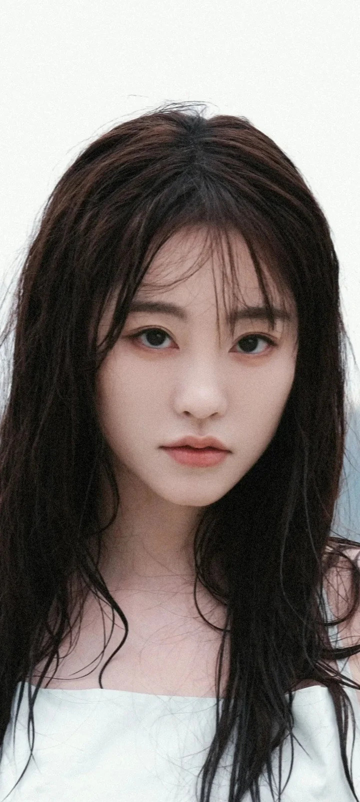 一位长发女性身穿白色露肩上衣，在浅色背景前面对镜头。
