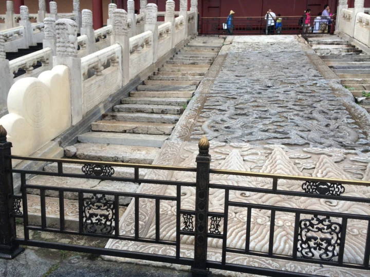 石雕龙纹台阶与白色石栏杆构成一处传统建筑细节，远处可见几位行人。