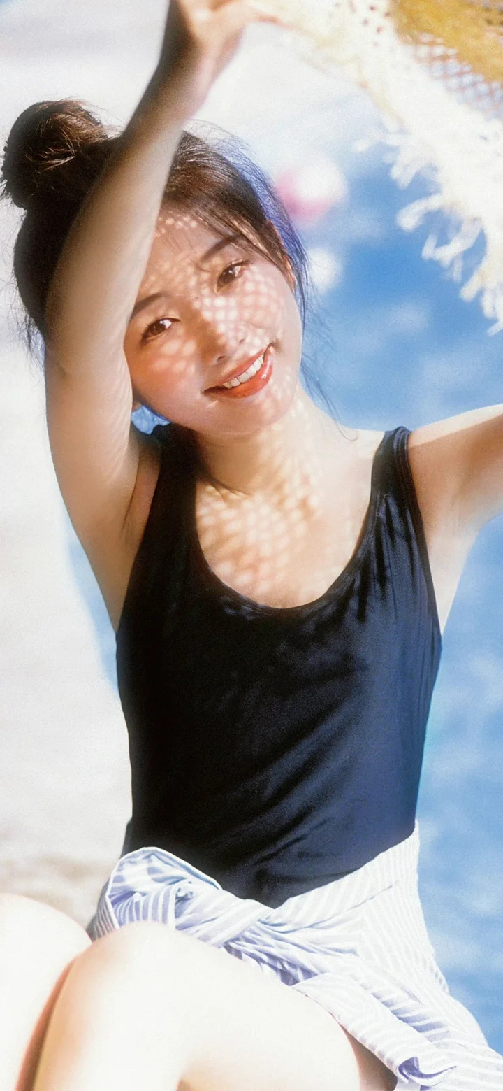 一名成年女性穿着黑色无袖上衣，在明亮阳光下微笑面对镜头。
