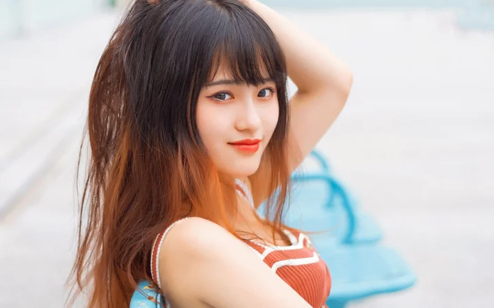 一位长发女性在明亮背景前抬手整理头发并面向镜头微笑。