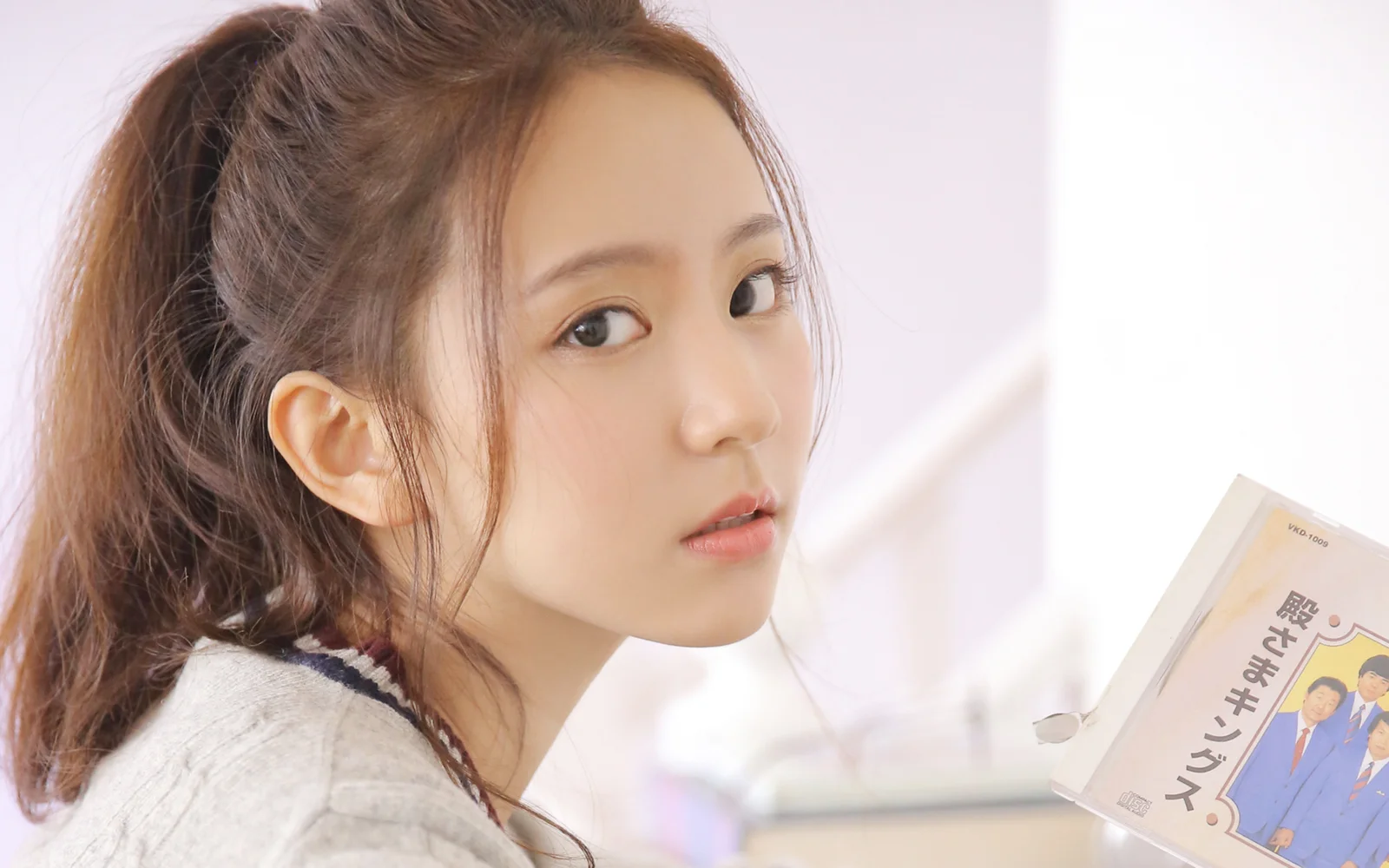一位成年女性在明亮的室内手持书本并回望镜头。