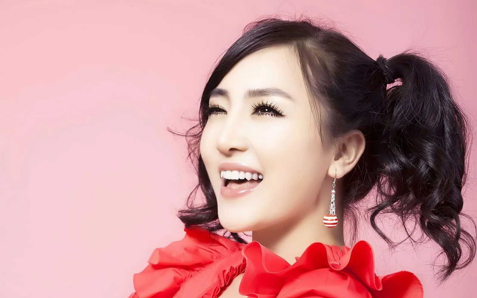 분홍색 배경 앞에서 빨간색 러플 상의를 입은 양갈래 머리의 성인 여성이 미소 짓고 있다.