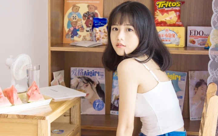 一名女性坐在摆放书籍和零食的木质书架前回头看向镜头。