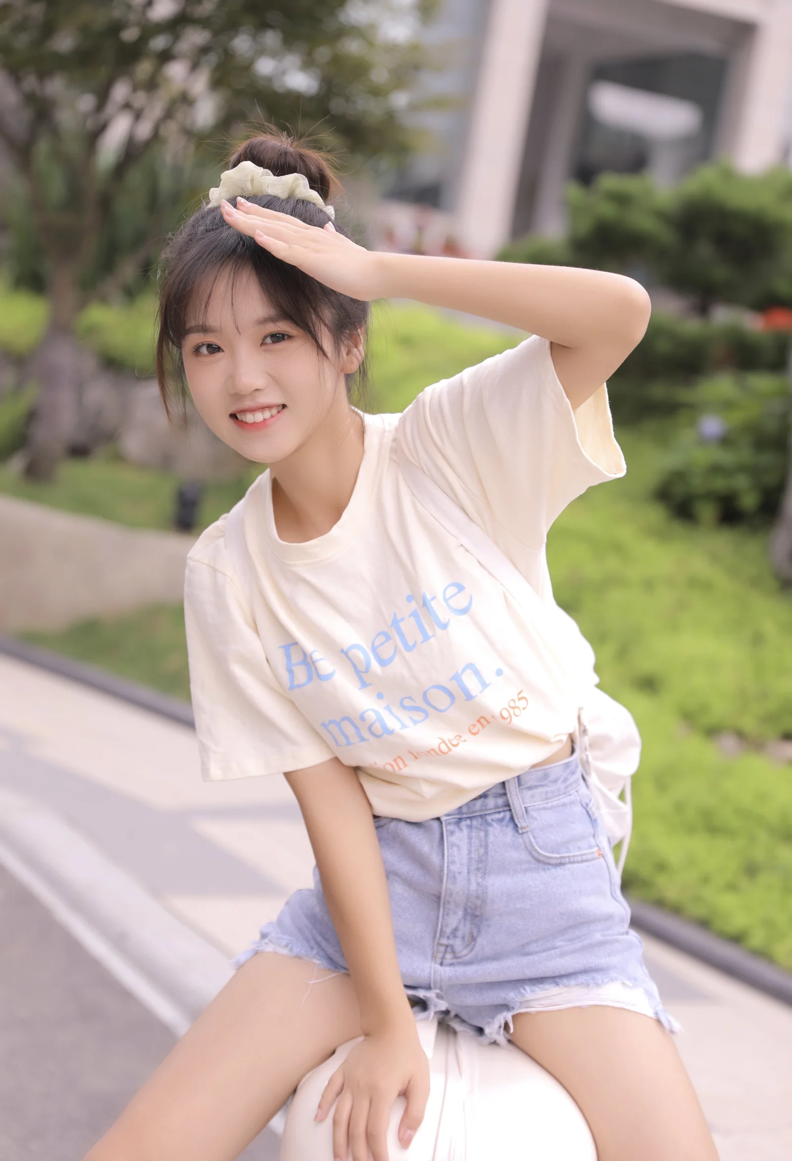一名微笑的女性坐在绿意盎然的户外环境中，抬手遮挡阳光。