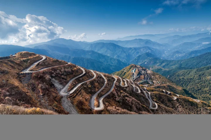 蜿蜒山路穿过起伏的山脉，远处是层叠的山谷和蓝天白云。