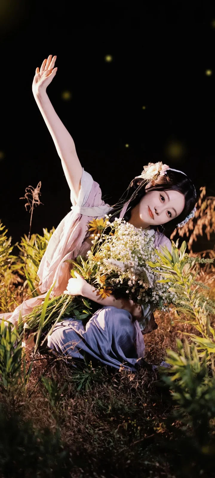 一名女性在花丛中手捧花束并抬起一只手。