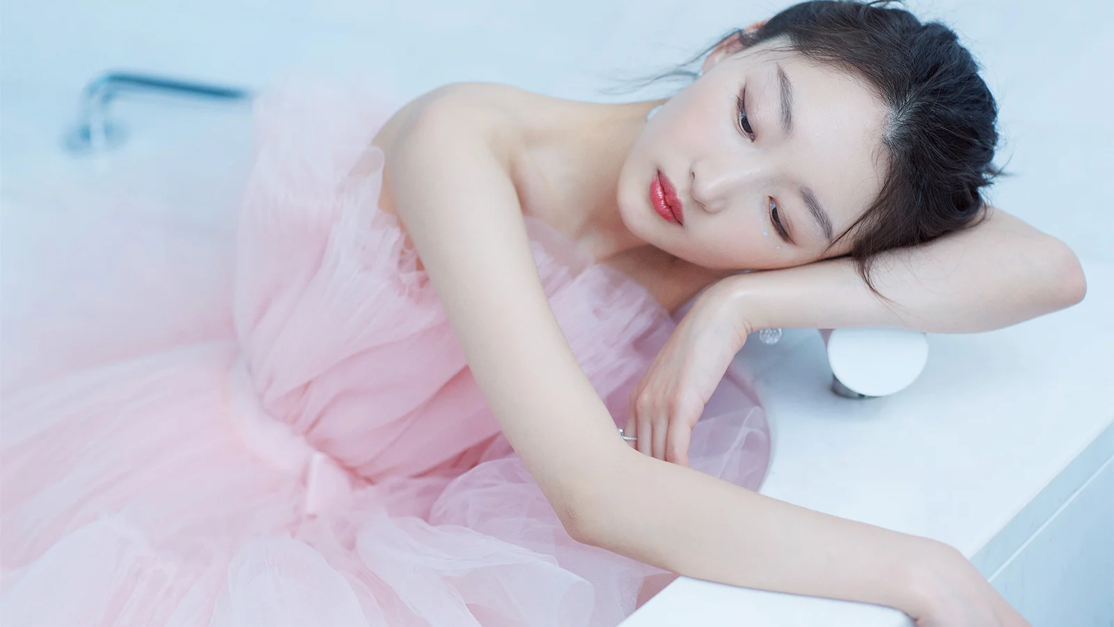 淡いピンクのチュールドレスを着た成人女性が、白い台の上に横たわっています。