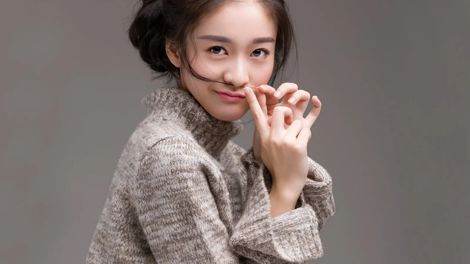 一名成年女性穿着灰色针织衫，在灰色背景前摆出自然姿态。