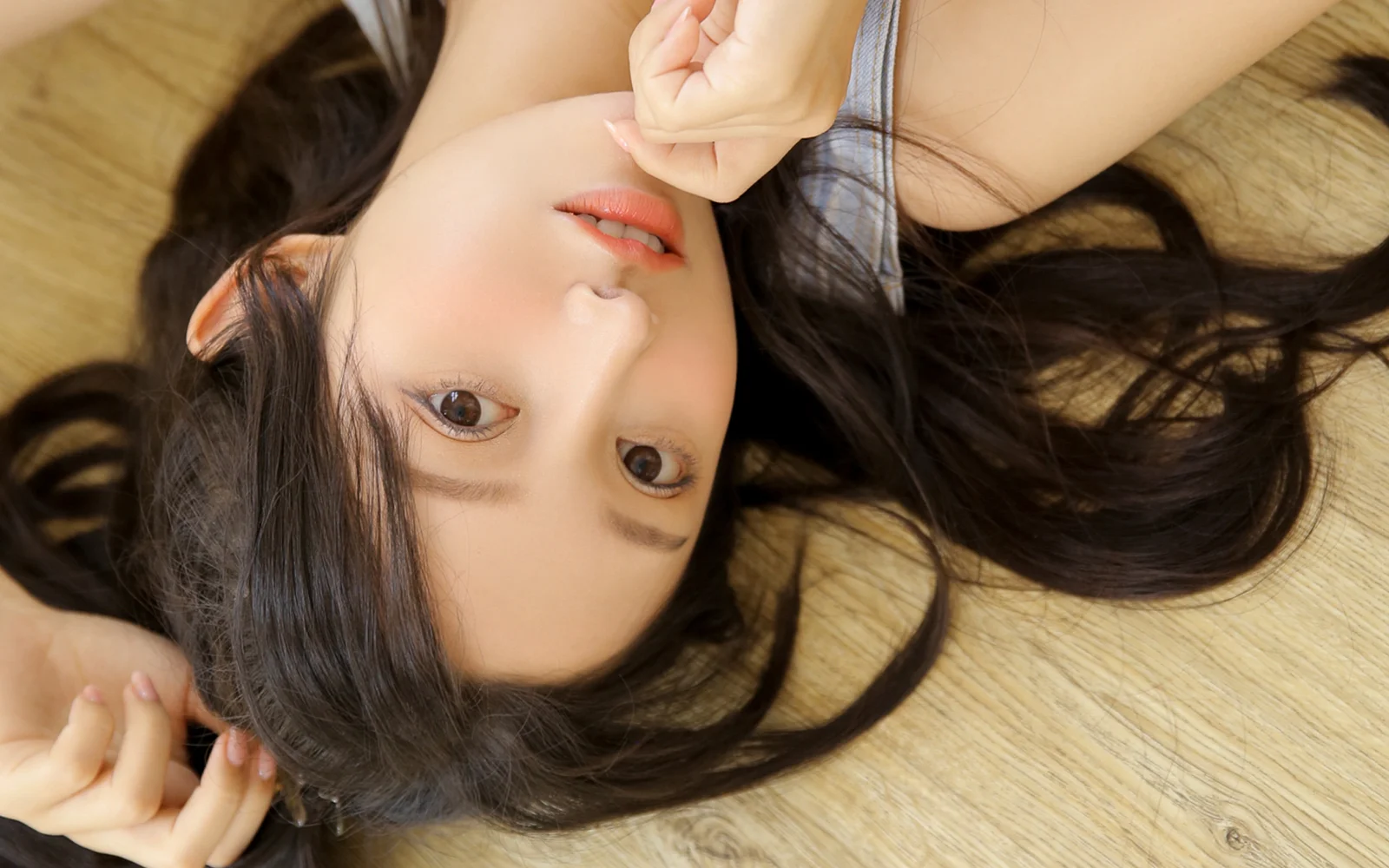 一名长发女性躺在木地板上直视镜头，画面呈横向构图。