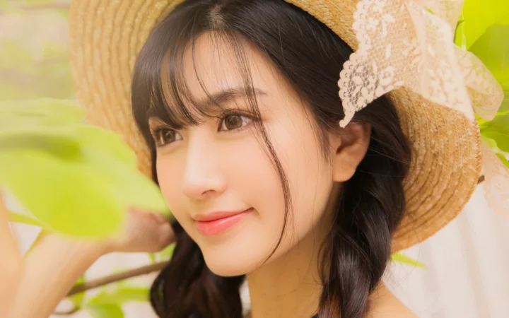 一位戴着草帽、留着编发的女性面部特写，背景是明亮的绿色叶片。