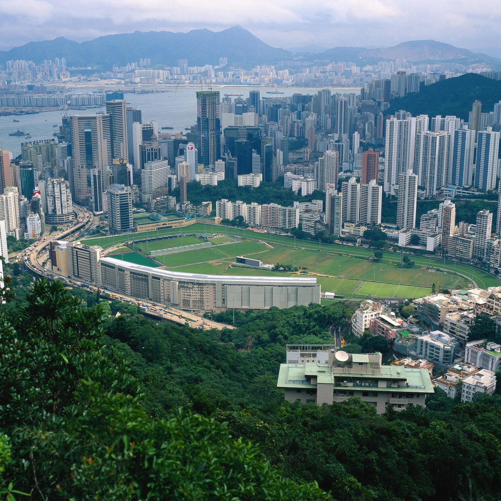 高处俯瞰城市高楼、海湾、体育场与远处山脉。