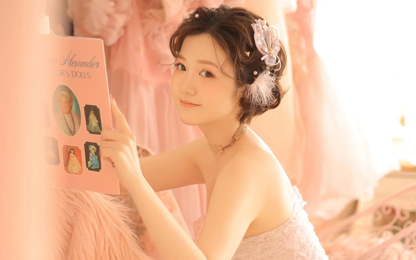 白いドレスを着た成人女性が、暖かな室内の光の中で本を手にカメラを振り返っています。
