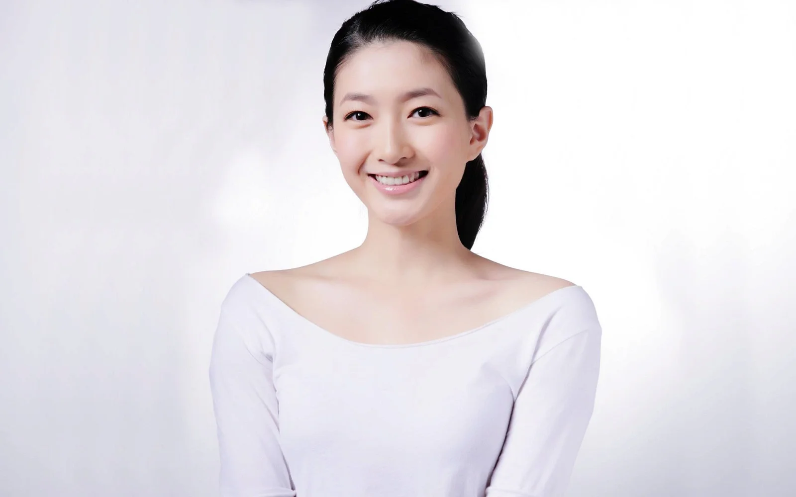 一名扎着马尾的成年女性穿着白色上衣，在浅色背景前微笑面对镜头。