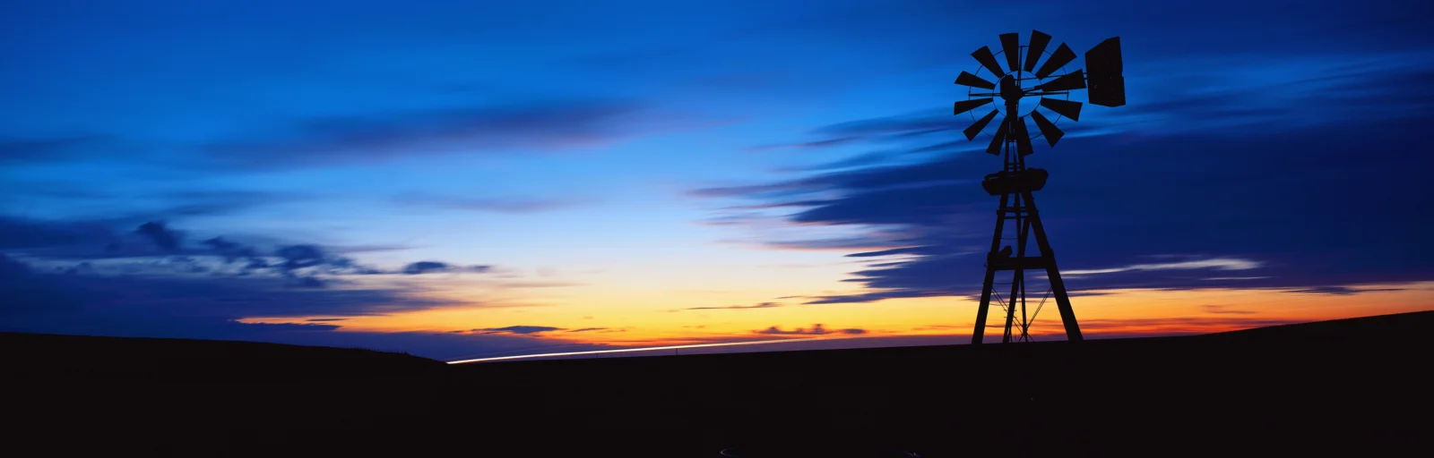 地平线上的风车剪影映衬着蓝橙交织的夕阳天空。