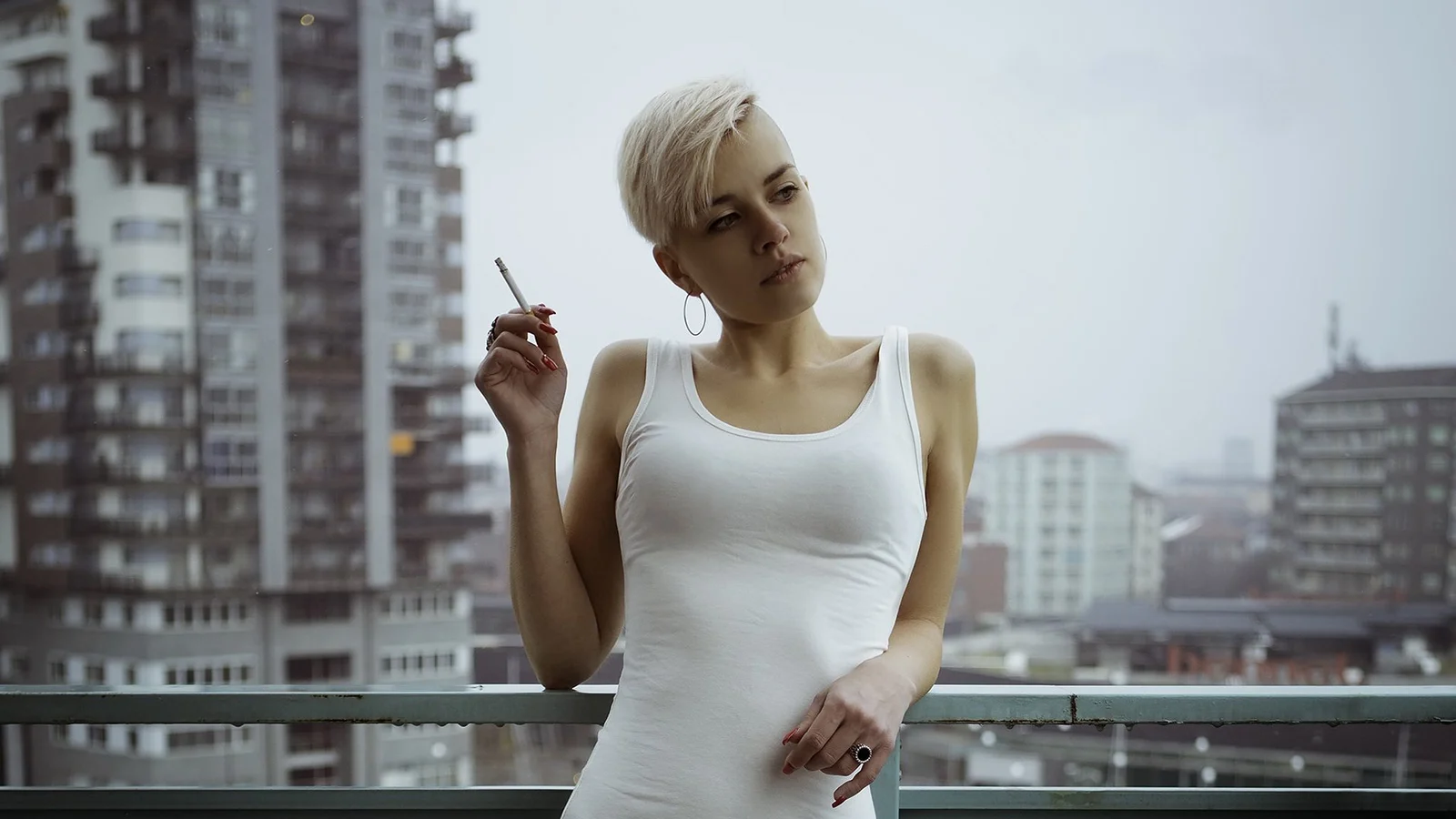 一名短髮女性站在城市陽台上，身後是朦朧的高樓建築。
