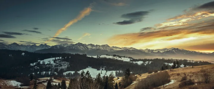 夕陽映照下的雪山、森林與起伏山坡構成壯麗的冬日全景。