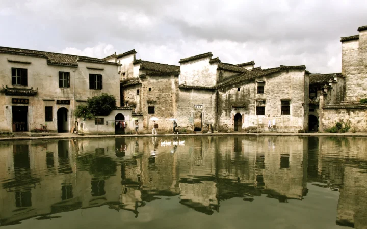 一排古朴的临水建筑倒映在平静的运河中，天空被厚重云层覆盖。