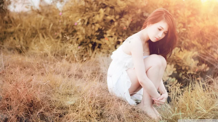 一名女子身穿白色连衣裙，坐在阳光洒落的草地上。