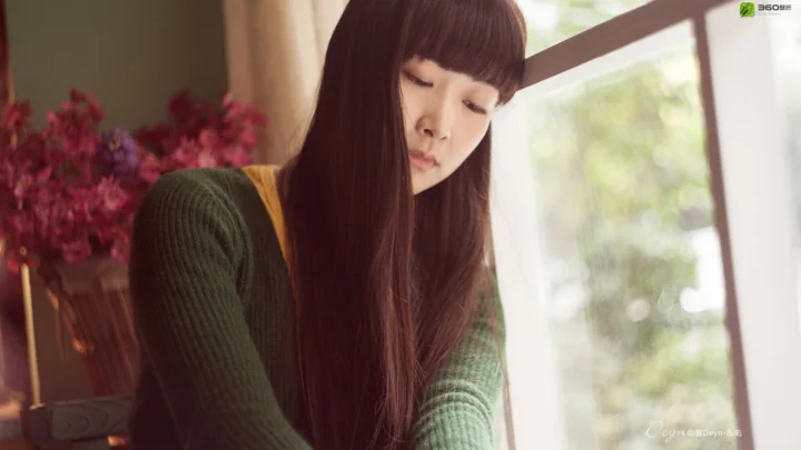 긴 머리의 여성이 부드러운 실내 조명 아래 창가에 앉아 있고 창밖으로 흐릿한 초록 풍경이 보입니다.