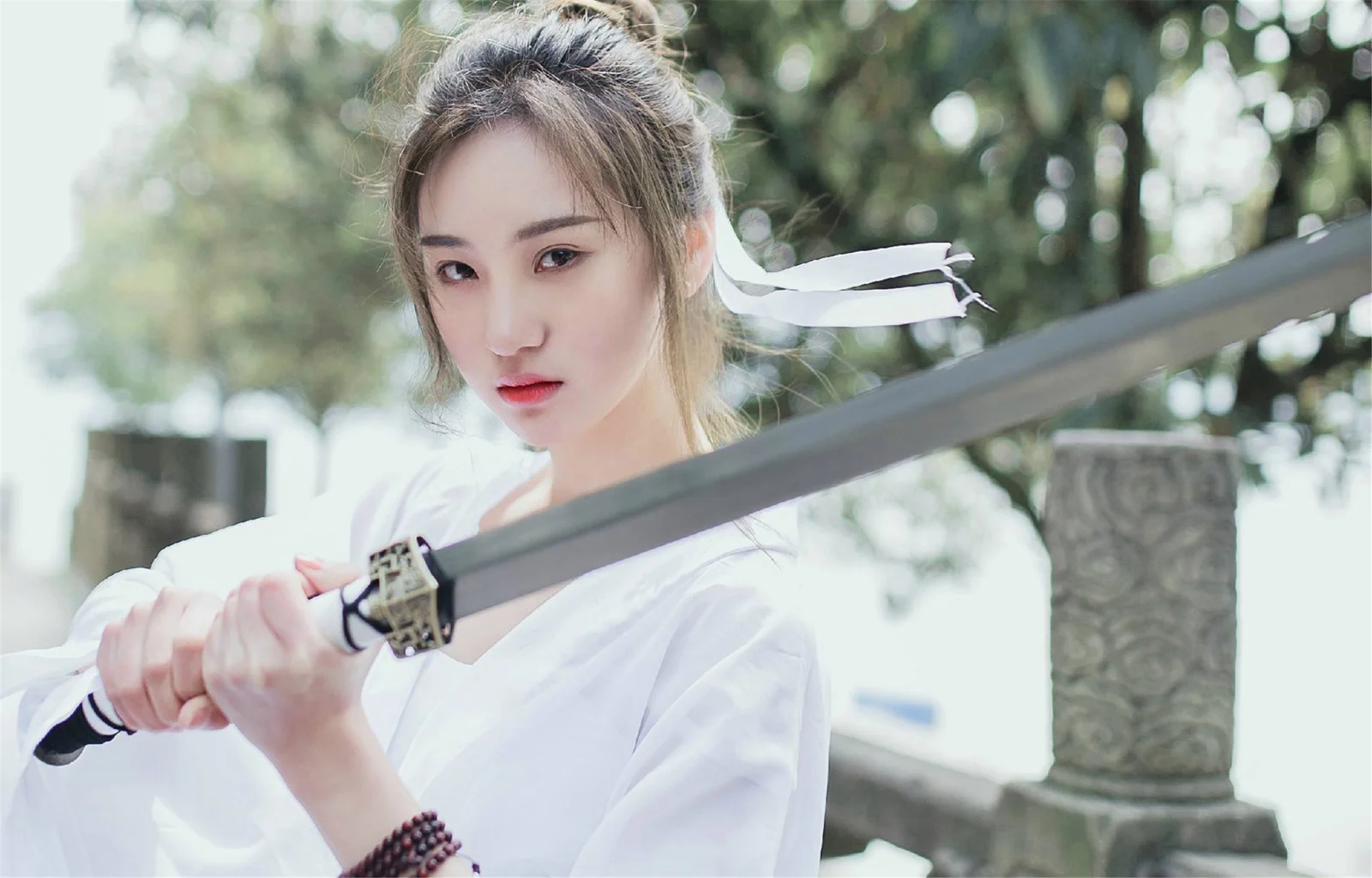 一名身穿白衣的女子在户外手持长剑面对镜头。